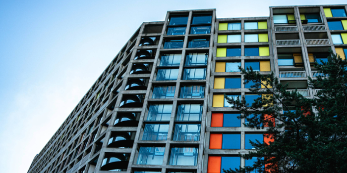 A brutalist high-rise apartment block made of concrete and glass. The windows are interspersed with bright panels in yellows and oranges.