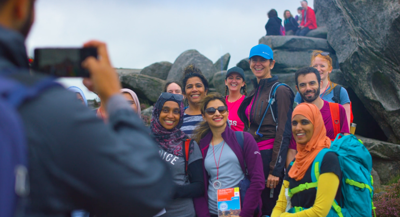A group of people, out walking, stop next to a rocky outcrop to have a photo taken.