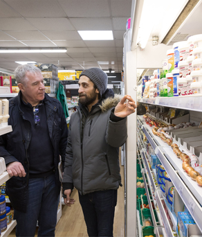 The inside of a food shop, with the owner and a customer standing between rows of shelves. 
