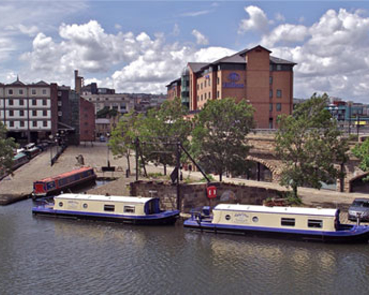 A view of Victoria Quays and the canal basin in the centre of Sheffield on a sunny day. There are several narrow boats moored up.