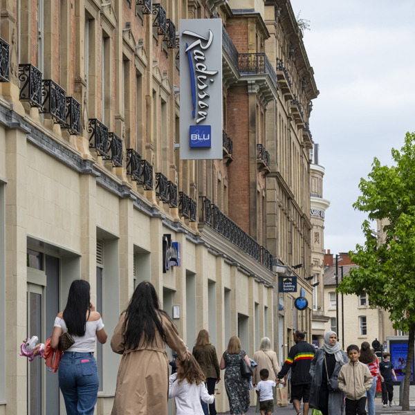 The exterior of the Radisson Blu Hotel on Pinstone Street in Sheffield city centre. The street is filled with people walking up and down. Above them hangs the Radisson Blu sign.
