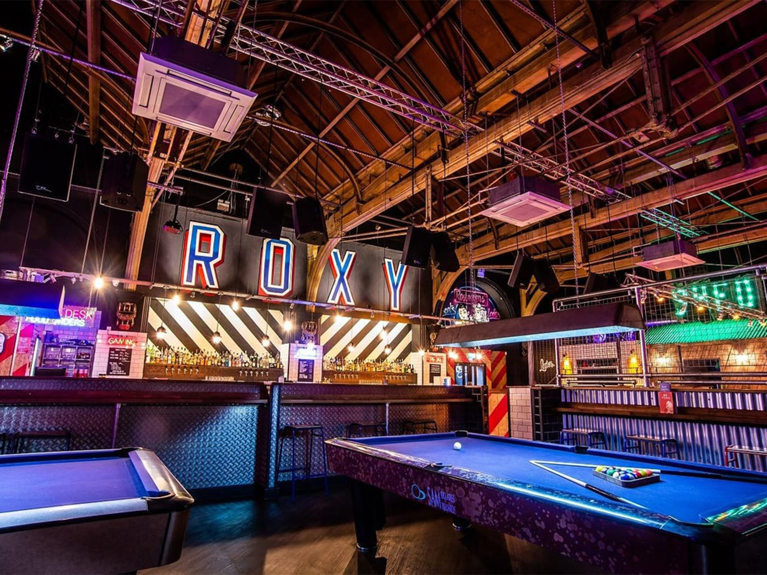 Interior of the Roxy Ball Room with bright neon lights, a bar and gaming tables.