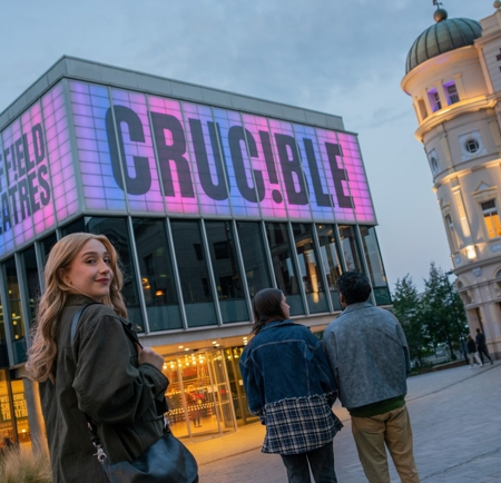 Sheffield Theatres’ Crucible building glowing pink at dusk, showing people arriving for an evening performance in the city centre.