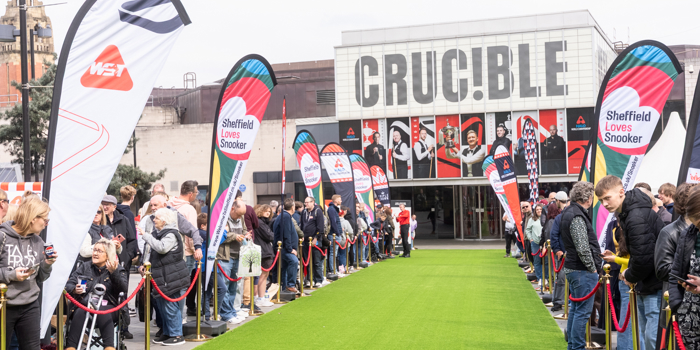 Crowds line a green carpet outside the Crucible Theatre for a Sheffield Loves Snooker event, with colourful flags and the theatre’s bold façade in the background.