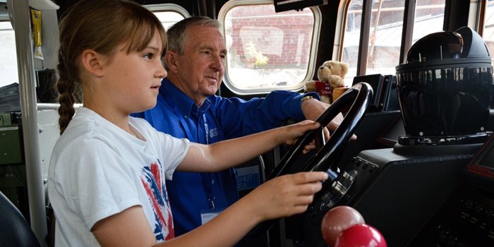 A child and an adult inside a lifeboat in a museum.
