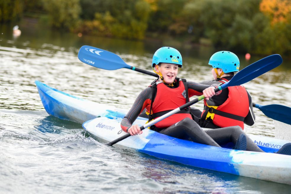 Two young people are having fun canoeing on a stretch of water in the countryside. 