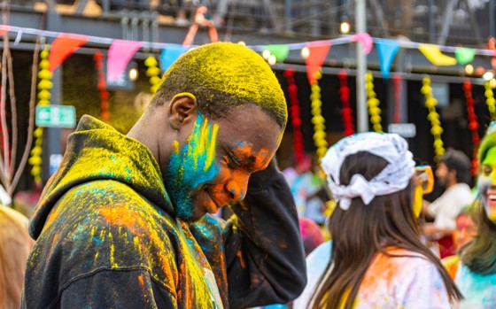 Person with bowed head covered in luminous paint at vibrant and colourful festival.