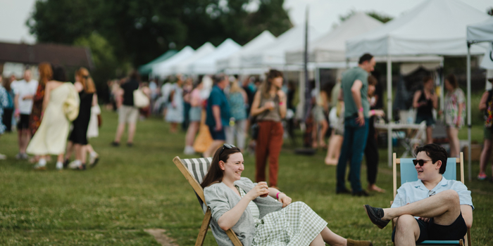 An outdoor event with lots of marquees, crowds of people walking about and some sitting in deck chairs.