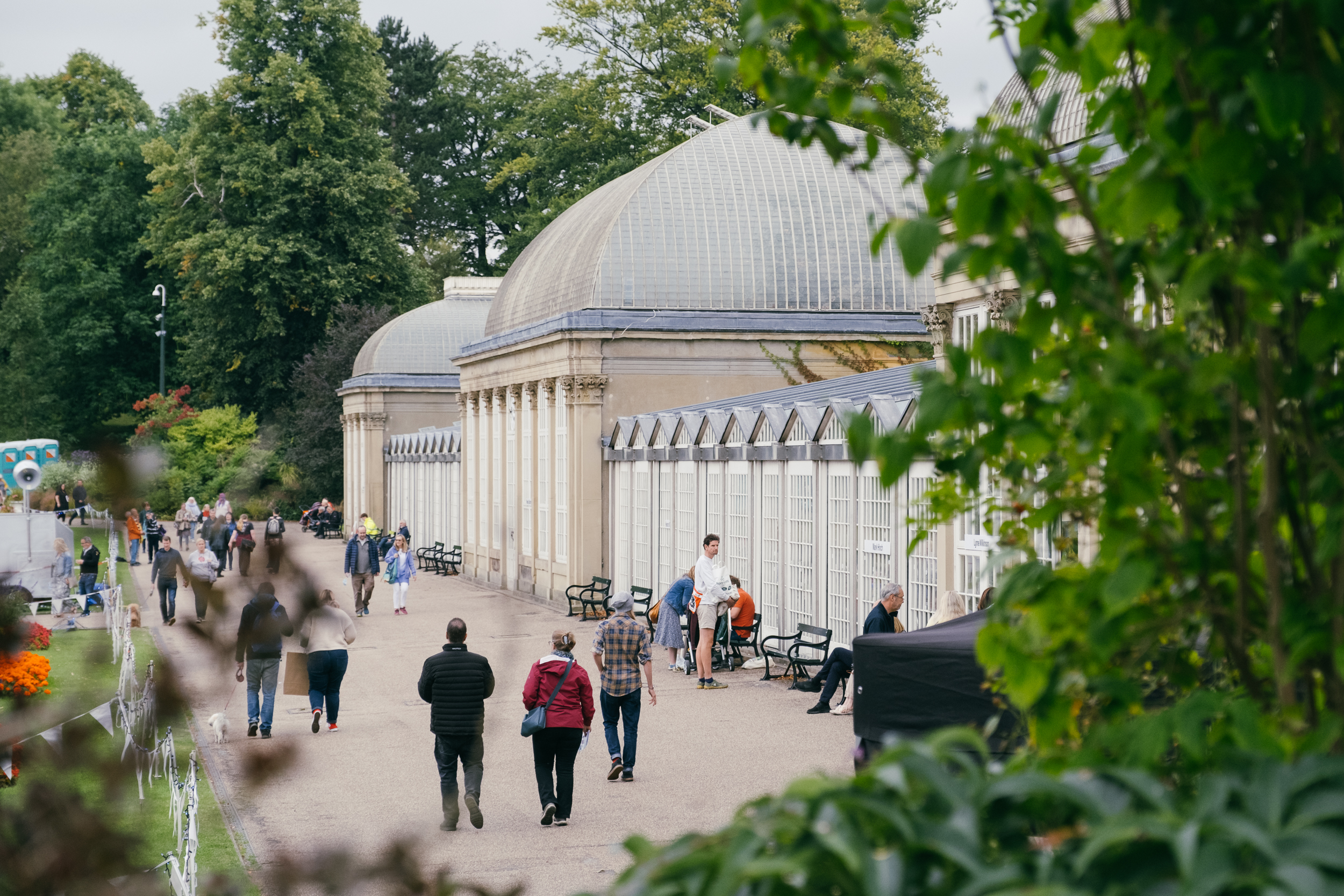 People are strolling along the wide path that runs along the length of the glass house in Sheffield Botanical Gardens.