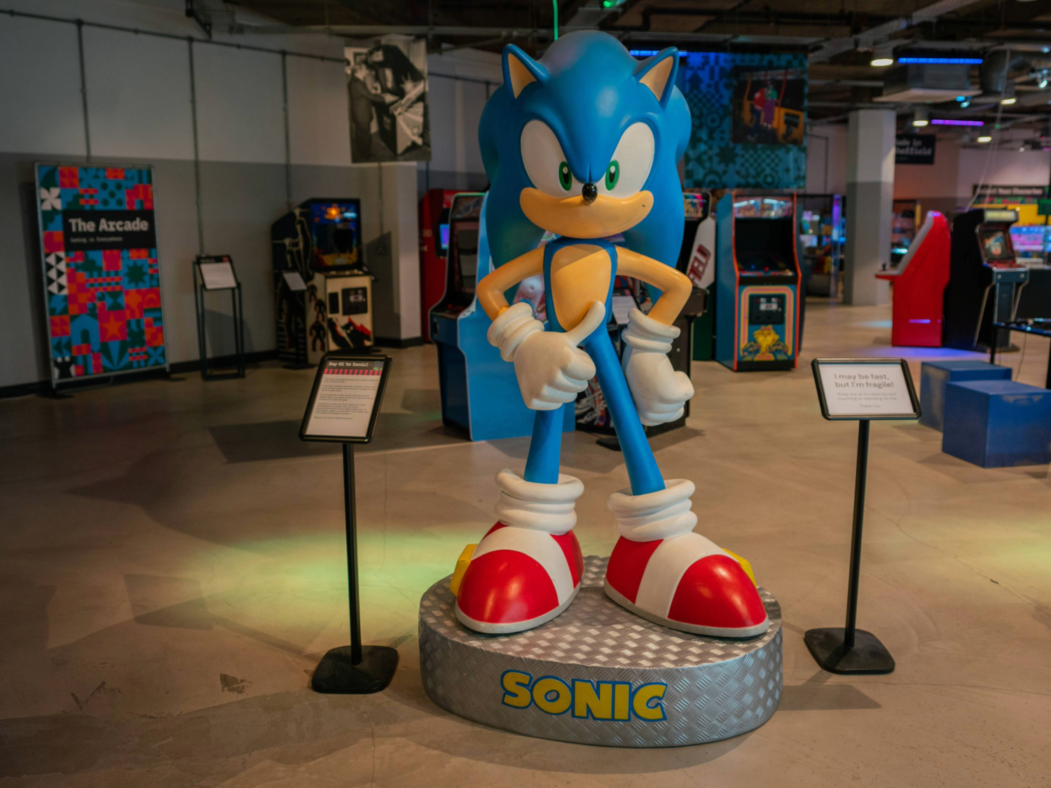 A large scale statue of the video game character Sonic the Hedgehog stands in the foreground. In the background are arcade game cabinets and other displays about video game history.