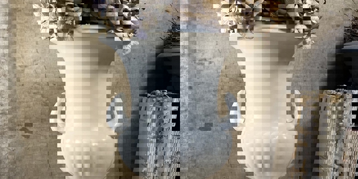 A white porcelain vase, in the style of a Greek urn, with dried flowers in.