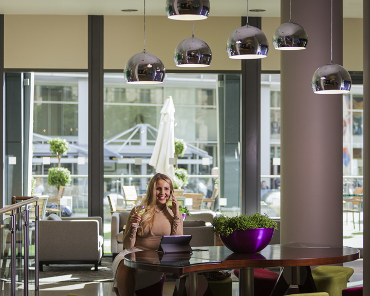 Female working in bar area with tables and chairs and overhead pendant lights.