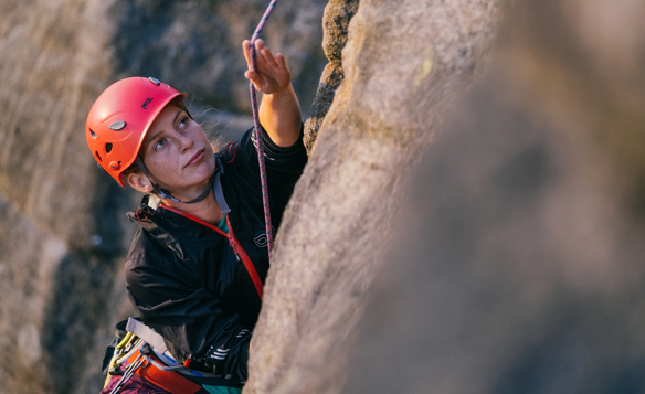 A woman climbing a gritstone rock face.