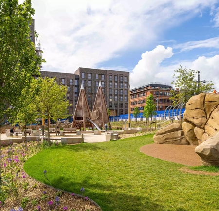 A grassy area in Pound's Park flanked by big boulders and play equipment.