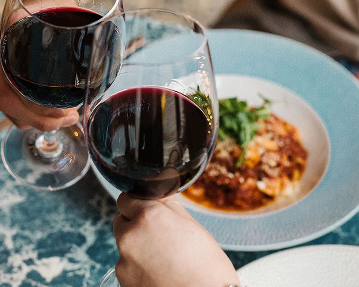 Two wine glasses clinking above plates of food.
