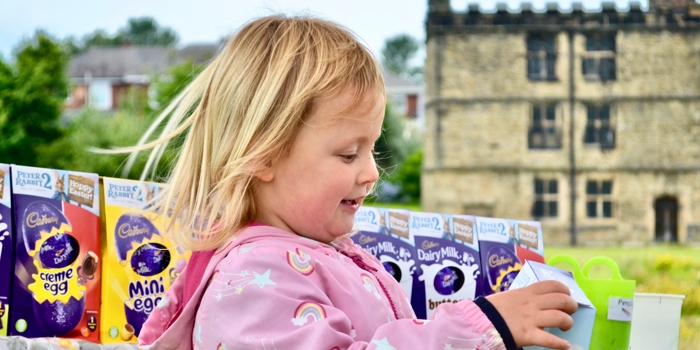 A child, standing in an outdoor setting, is holding a chocolate Easter egg in a box.