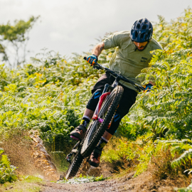 Male mountain biker riding through a dirt track in a leafy setting.
