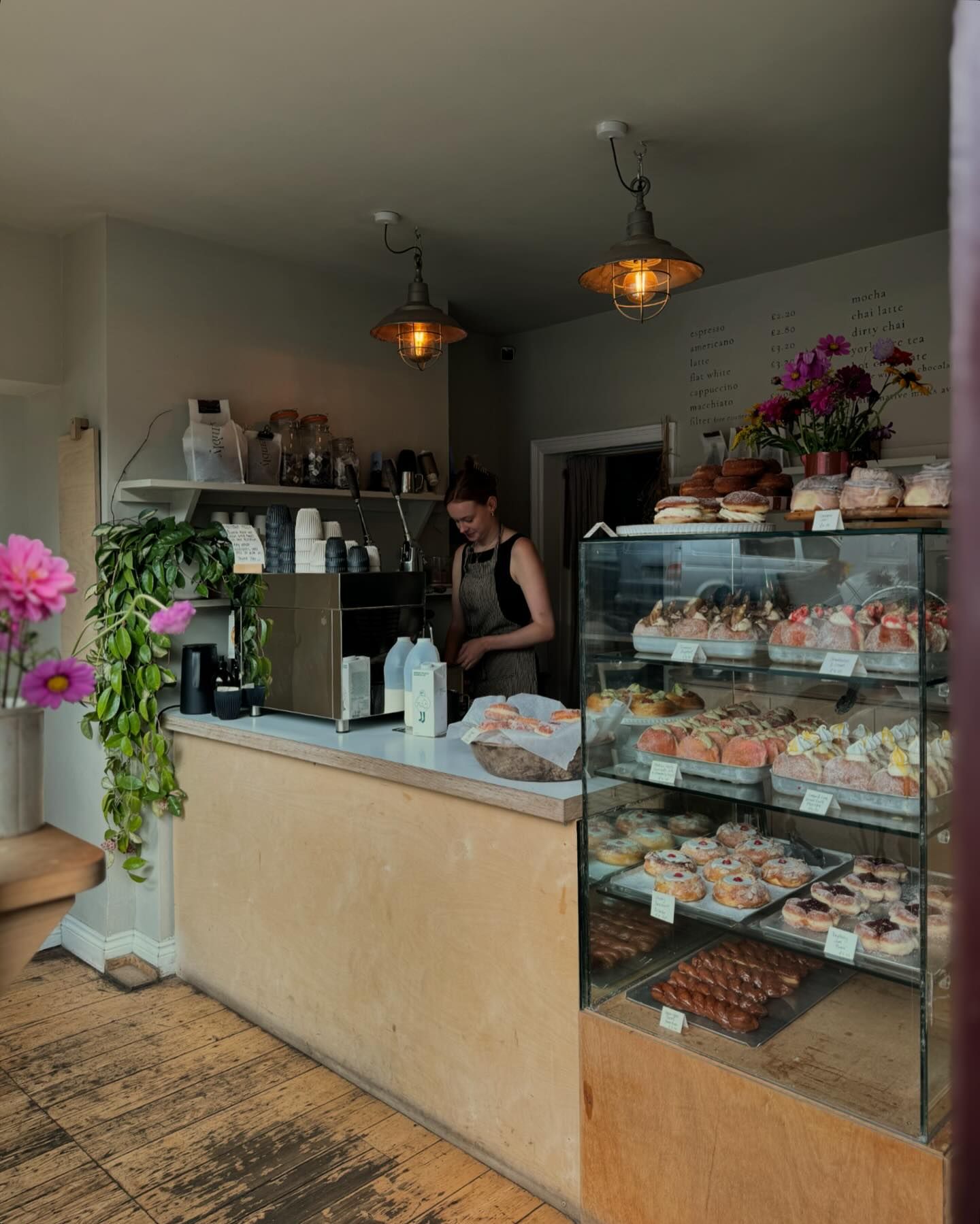 Insides Eve Kitchen. A person stands behind the counter. Inside a glass display case is a range of pastries and cakes.