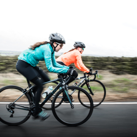 Two female cyclists riding their bikes in the countryside, the background is blurred as they speed past.