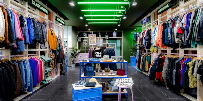 Inside the Glass Onion shop. All the walls are full of clothes on rails. In the centre of the shop are tables with accessories on display.