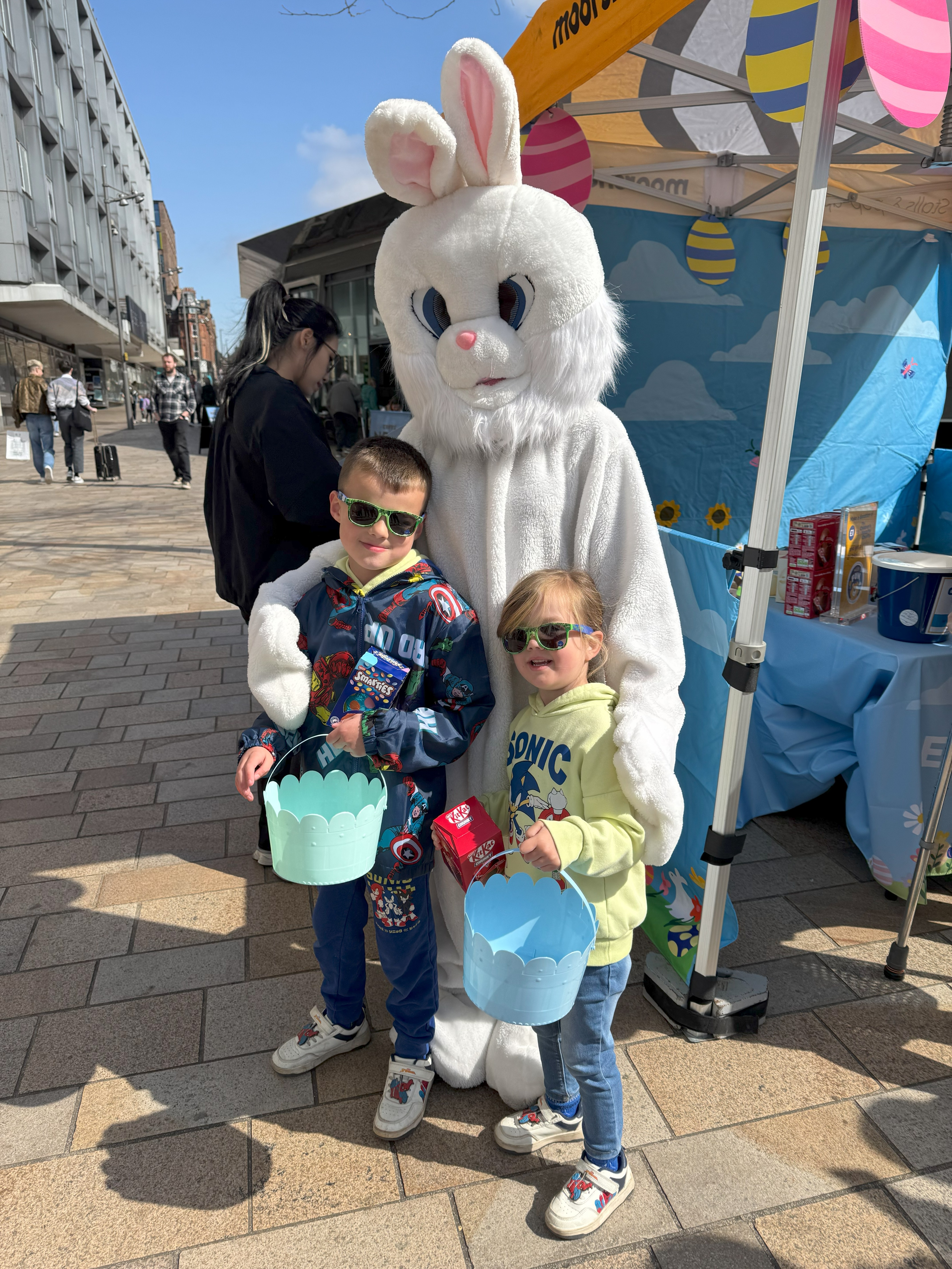 Two children posing for a photo with a person dressed as the Easter Bunny on The Moor.