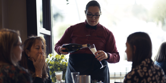 A member of staff pours sparkling wine for a table of guests at Nonnas Restaurant.