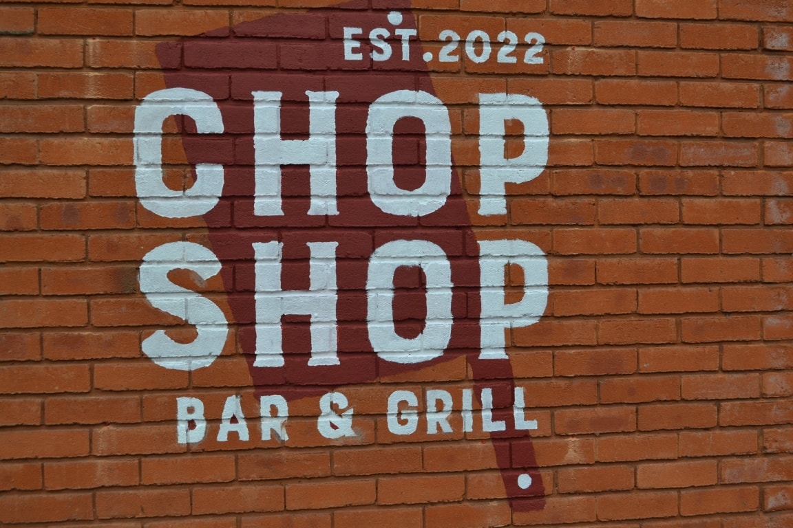 The Chop Shop Bar & Grill logo painted on a red brick wall.
